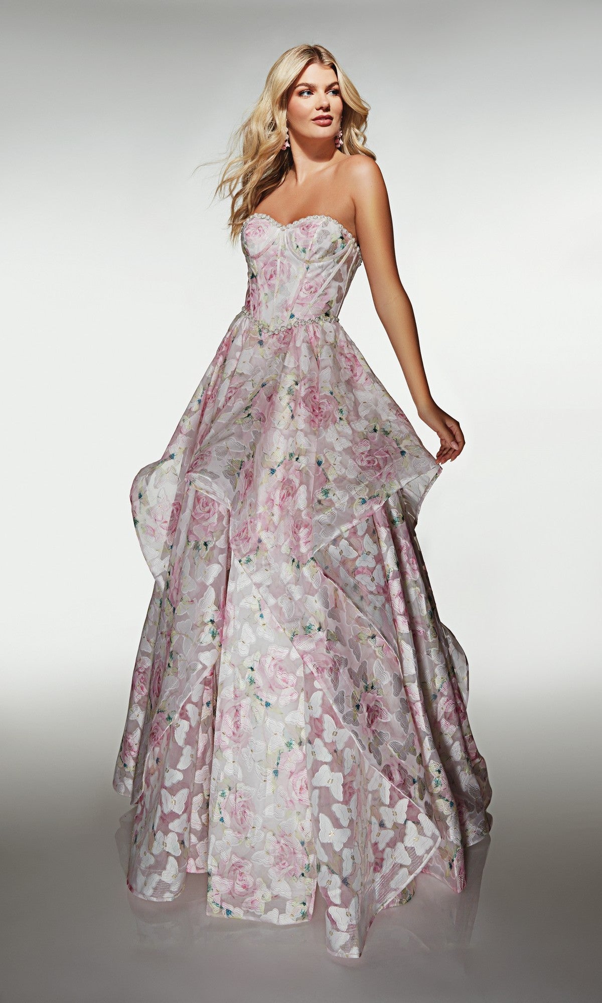 A woman poses in the Alyce 62071 Long Prom Dress, a strapless organza ball gown with a pastel floral pattern and a layered, flowing skirt, set against a plain background.